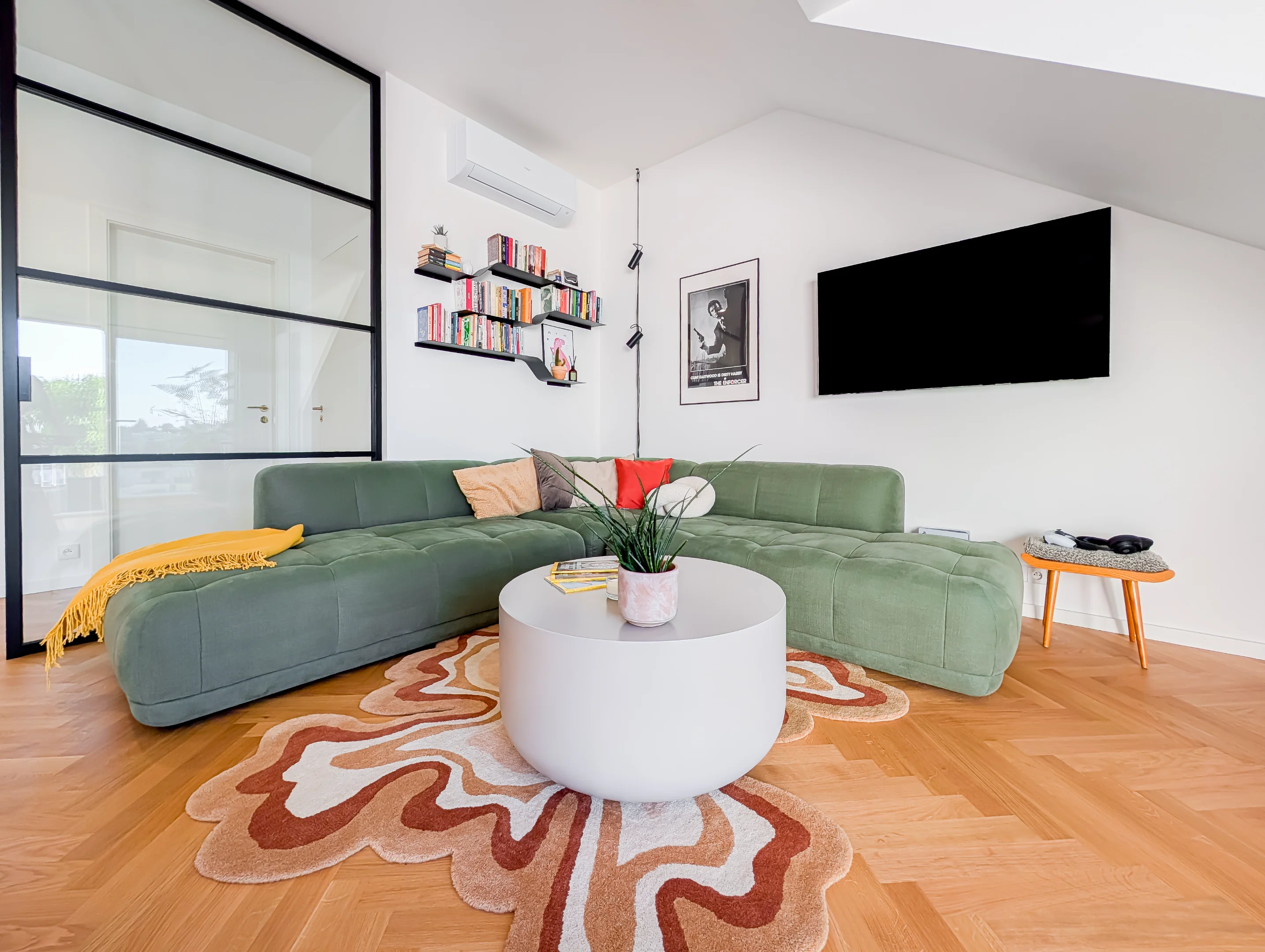 Zelená sedačka, bílý stůl a designový koberec v obýváku.